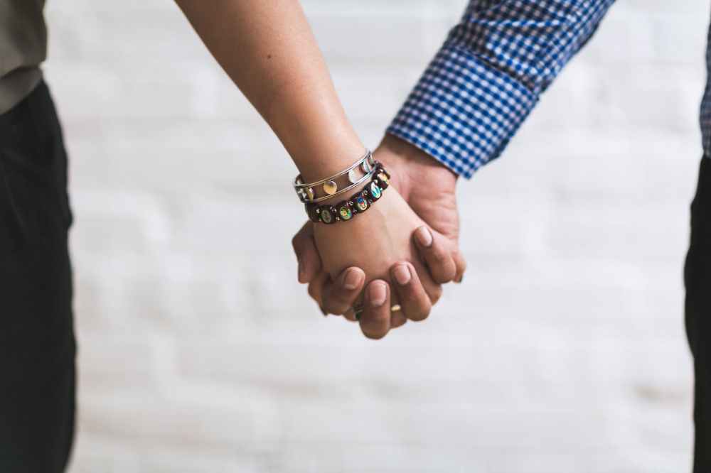couple holding hands near white painted wall